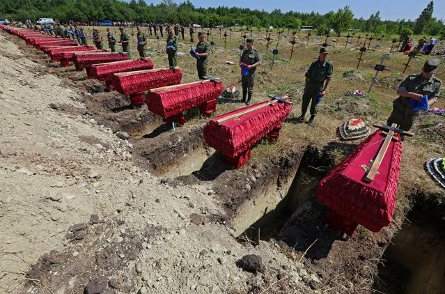 Service members stand near the coffins during a funeral for 58 unidentified soldiers of the self-proclaimed Luhansk People's Republic who were killed in 2022 during Ukraine-Russia conflict, in Luhansk, Ukraine on July 12, 2022. (Photo by Alexander Ermochenko/Reuters)