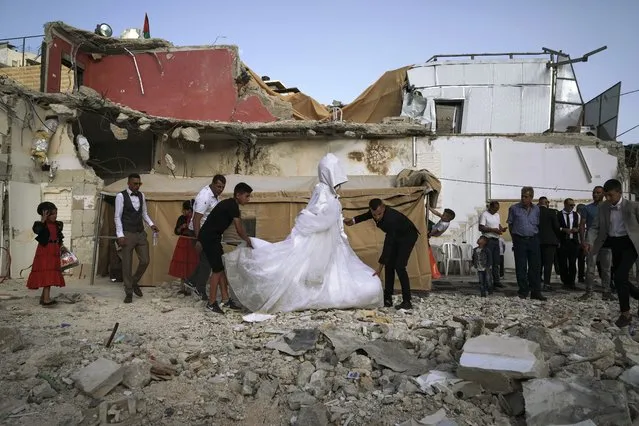 Palestinian bride Rabiha al-Rajby and groom Mohyeldin Nasrallah start their wedding ceremony from the ruins of al-Rajby's home in east Jerusalem neighborhood of Silwan, Saturday, June 11, 2022. Israeli authorities demolished the building, displacing its 35 residents, last month, saying it was built without municipal permit as part of the wider struggle between the city and Palestinian residents. (Photo by Mahmoud Illean/AP Photo)