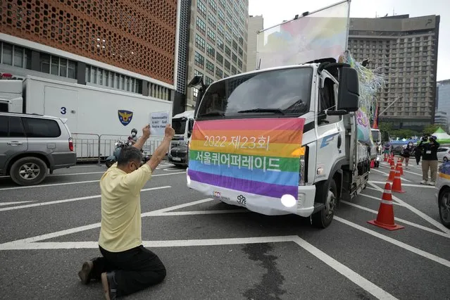 A protester holds a sign as he kneels down in front of parade trucks before a parade as a part of the 23rd Seoul Queer Culture Festival which is held from from July 15 to July 31, in Seoul, South Korea, Saturday, July 16, 2022. Thousands of gay rights supporters marched under a heavy police guard in the South Korean capital on Saturday as they celebrated the city's first Pride parade in three years after a COVID-19 hiatus. The flag on the truck reads “The 23rd Seoul Queer Parade”. (Photo by Lee Jin-man/AP Photo)