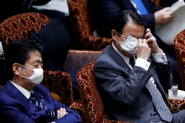 Japan's Finance Minister Taro Aso, next to Japan's Prime Minister Shinzo Abe, adjusts his protective face mask during an upper house parliamentary session, following an outbreak of the coronavirus disease (COVID-19), in Tokyo, Japan April 1, 2020. (Photo by Issei Kato/Reuters)