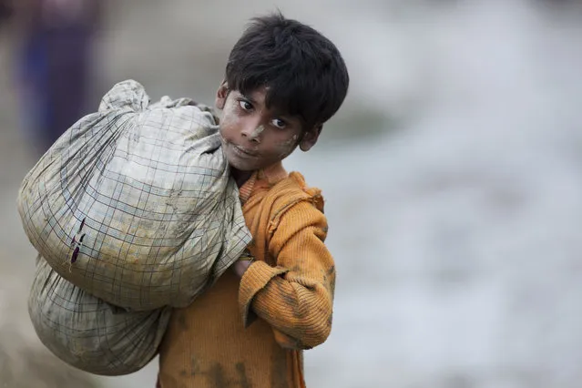 In this Wednesday, September 20, 2017 photo, a Rohingya Muslim boy walks carrying belongings near Balukhali refugee camp in Cox's Bazar, Bangladesh. Children make up about 60 percent of the sea of humanity that has poured in to Bangladesh over the last four weeks fleeing terrible persecution in Myanmar. And the U.N.’s child rights agency UNICEF has so far counted about 1,400 children who have crossed the border without their parents. (Photo by Bernat Armangue/AP Photo)