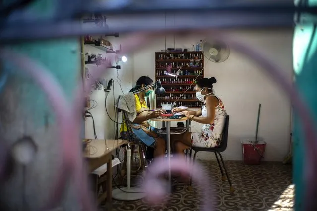 Two women wearing masks as a precaution against the spread of the new coronavirus paint their nails at a home nail salon in Havana, Cuba, Tuesday, March 31, 2020. Cuban authorities are requiring the use of masks for anyone outside their homes. (Photo by Ramon Espinosa/AP Photo)