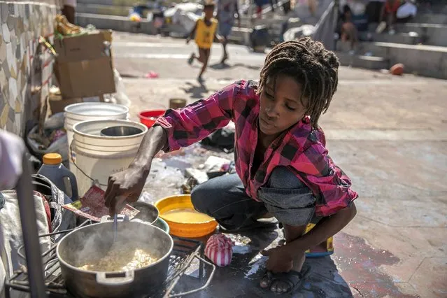A woman stirs a pot of food at the Hugo Chavez public square transformed into a refuge for families forced to leave their homes due to clashes between armed gangs in Port-au-Prince, Haiti, Thursday, October 20, 2022. (Photo by Joseph Odelyn/AP Photo)