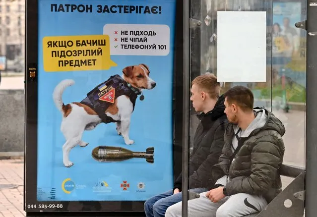 People look at a poster depicting Patron, a Jack Russell Terrier renowned for helping sappers demine areas recaptured from Russian forces, reading “Patron warns. If you see a suspicious object, do not approach, do not touch, call 101”, at a bus stop in central Kyiv on October 24, 2022. Patron, who has more than 290,000 followers on Instagram, received a medal for Dedicated Service from Zelensky in May and was awarded a special prize at the Cannes Film Festival. (Photo by Sergei Supinsky/AFP Photo)