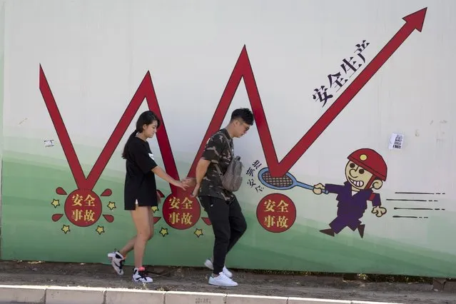 A couple walks in front of a work safety propaganda billboard in Beijing, China, Thursday, August 25, 2016. Work safety, which has long been sidelined by China's pursuit of profits and economic growth, kills tens of thousands each year. Chinese character at right reads “Safe Production”. (Photo by Ng Han Guan/AP Photo)