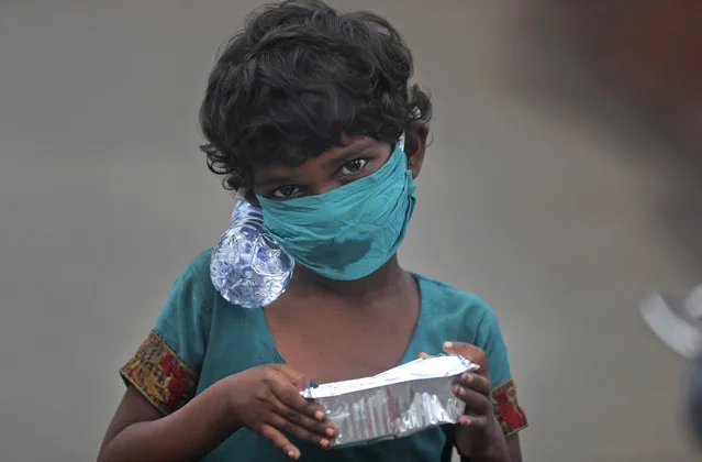 A girl wearing a face mask walks with a bottle of drinking water and a food packet that she received from a food distribution site in Mumbai, India, Saturday, June 20, 2020. India is the fourth hardest-hit country by the COVID-19 pandemic in the world after the U.S., Russia and Brazil. (Photo by Rafiq Maqbool/AP Photo)