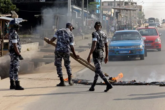 Policemen remove a barricade set on fire by demonstrators to block a road during a protest against president Alassane Ouattara's decision to stand for a third term, in Abidjan, Ivory Coast, August 13, 2020. (Photo by Luc Gnago/Reuters)