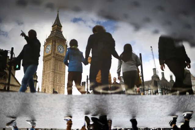 The Elizabeth Tower, more commonly known as Big Ben, is seen reflected in a puddle as people walk outside the Houses of Parliament in London, Britain on October 23, 2022. (Photo by Henry Nicholls/Reuters)