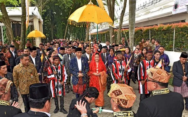 This handout released on November 25, 2017 shows Indonesia' s President Joko Widodo (L under umbrella) and First Lady Iriana Widodo (R under umbrella) arriving for their daughter' s wedding procession in Medan Widodo and his family took part in traditional Batak Mandailing customs as part of wedding festivities for his daughter Kahiyang Ayu Siregar' s marriage to Bobby Siregar in Siregar' s hometown of North Sumatra. (Photo by Agus Suparto/AFP Photo/Indonesian Presidential Palace)