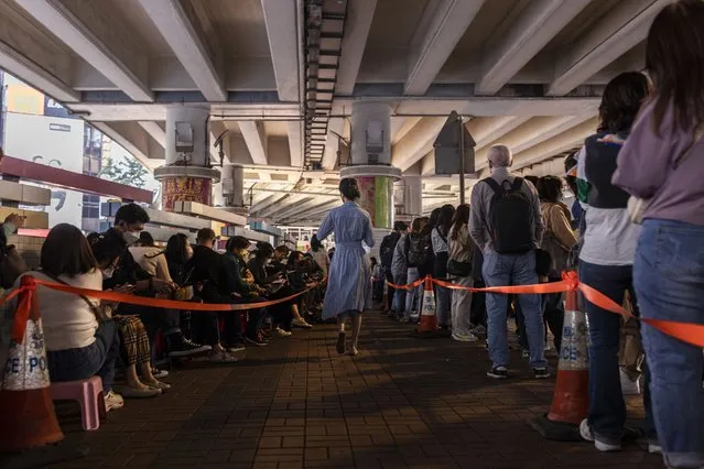 A pedestrian passes lines of customer waiting to receive a “villain hitting” ceremony on the day of “ging zat”, as pronounced in Cantonese, which on the Chinese lunar calendar literally means “awakening of insects”, under the Canal Road Flyover in Hong Kong on Monday, March 6, 2023. (Photo by Louise Delmotte/AP Photo)