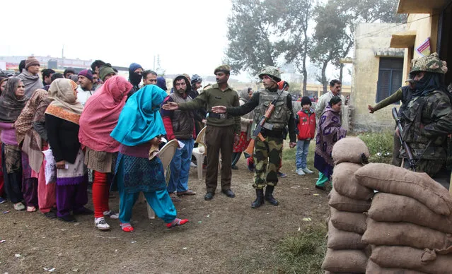 Indian paramilitary soldiers stand guard, as people stand in queues to cast their votes outside a polling station during the fifth phase of voting, at Satrayan village near the India-Pakistan international border, about 32 kilometers from Jammu, India, Saturday, December 20, 2014. The fifth and last stage of polling is being held in Jammu and Kashmir state and Jharkhand. (Photo by Channi Anand/AP Photo)