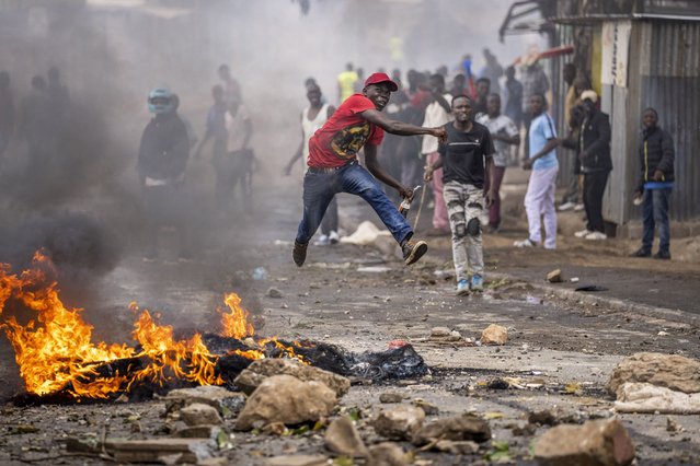 A protester jumps in the air as he throws a rock towards police next to a burning barricade in the Kibera slum of Nairobi, Kenya, Monday, March 20, 2023. (Photo by Ben Curtis/AP Photo)