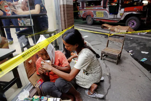 A street vendor is comforted at the scene where a man was killed shortly before midnight by unknown gunmen in Manila, Philippines early October 18, 2016. (Photo by Damir Sagolj/Reuters)