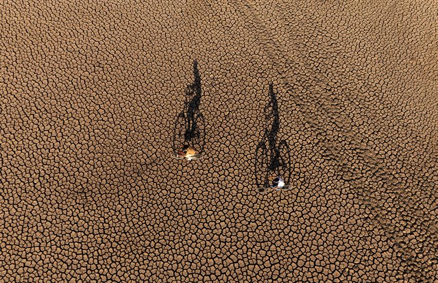 An aerial view of bicycle riders on dried up pond due to prolonged drought and extreme heat in Kocakent neighborhood of Mazidagi district in Mardin, Turkiye on July 04, 2025. With temperatures exceeding 40 degrees Celsius in the region, leaks at the bottom of the pond caused the water level to drop rapidly. Now entirely dried up, the pond once a fishing spot for both locals and visitors from nearby provinces has lost its function. Villagers stated that the pond had been both a source of livelihood and a social gathering place for years, expressing deep concern over the severe impact of the drought. (Photo by Mustafa Kilic/Anadolu via Getty Images)