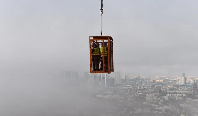 Journalists hang in a cage over fog covered Frankfurt am Main to watch the construction site of the Henninger tower in Frankfurt am Main, central Germany, on December 8, 2015. (Photo by Arne Dedert/AFP Photo/DPA)