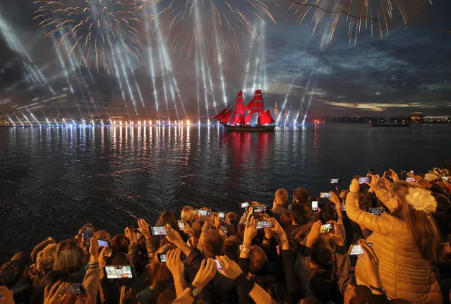 People watch a brig with scarlet sails on the Neva River during the Scarlet Sails festivities marking school graduation in St. Petersburg, Russia, early Sunday, June 24, 2018. This week graduation ceremonies and celebrations are held all over Russia as students of elementary and high schools and military academies finished their education. (Photo by Dmitri Lovetsky/AP Photo)