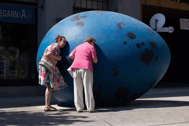 People listen to “The Hatchling. Song Thrush” – acoustic sculpture – scaled-up egg that make chick sounds like just before it hatches – by Polish artist Joanna Rajkowska at five corners square in Warsaw on June 8, 2023. (Photo by Wojtek Radwanski/AFP Photo)