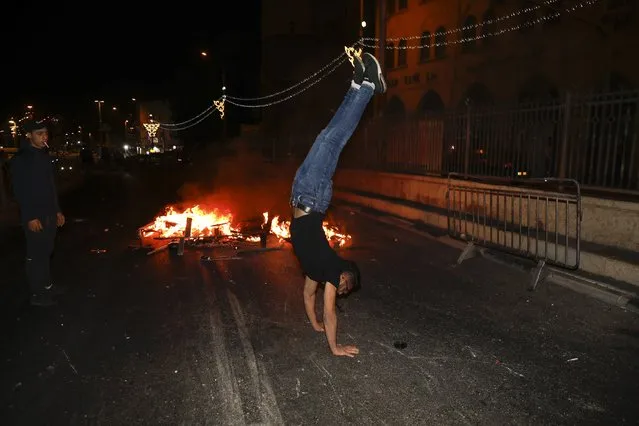 A Palestinian protester does a handstand next to a fire which was set on a road during clashes with Israeli police near Damascus Gate just outside Jerusalem's Old City, Sunday, May 9, 2021. Israeli police have been clashing with Palestinian protesters almost nightly in the holy city's worst religious unrest in several years. (Photo by Ariel Schalit/AP Photo)