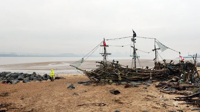 A man walks his dog by the Black Pearl driftwood pirate ship on the beach of the River Mersey at New Brighton in north west England on January 19, 2016. The ship was created by local artists Major Mace and Frank Lund from driftwood and was almost destroyed during the storms of 2013. (Photo by Paul Ellis/AFP Photo)