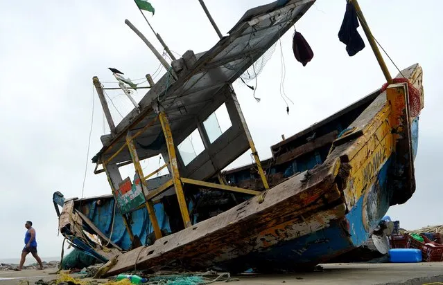 A man walks past a damaged fishing boat on a shore after heavy winds caused by Cyclone Tauktae, in Mumbai, India, May 18, 2021. (Photo by Hemanshi Kamani/Reuters)