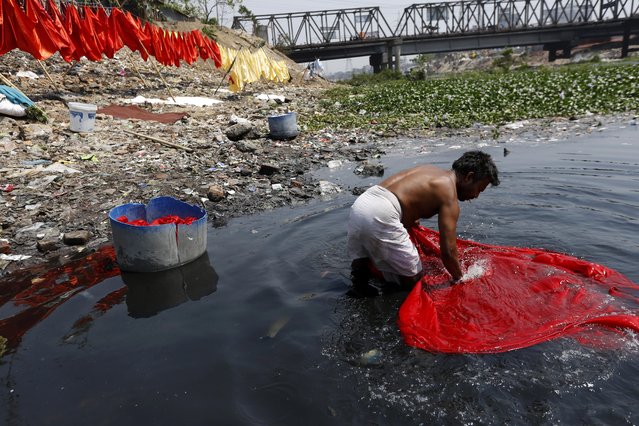 A washerman cleans clothes with polluted water in the river Buriganga in Dhaka, Bangladesh 22 March 2015. A large swathe of the Buriganga River which is the lifeline of the capital has turned pitch-black with toxic waste, oil and chemicals flowing into it from industrial units. The water became extremely polluted and represents a health hazard for the riverbed communities. (Photo by Abir Abdullah/EPA)