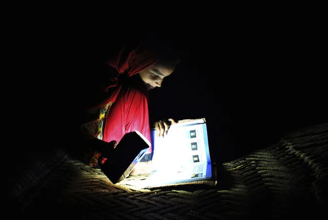 In this Friday, August 10, 2018, photo, Ansa Khan studies with a flash light during a power outage in Mardan, Pakistan. Ansa enjoys her school, saying her favorite subject is Islamiat. Electricity is not always reliable in Ansa’s Toru village and she is often forced to study by flashlight. (Photo by Saba Rehman/AP Photo)