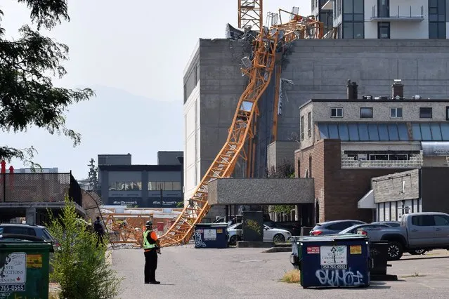 A worker looks on as a police officer investigates a collapsed crane resting on the building it damaged in Kelowna, Brith Columbia, Monday, July 12, 2021. Five people died when a crane toppled off a 25-story residential tower in Canada, police said Tuesday.  (Photo by Alistair Waters/The Canadian Press via AP Photo)