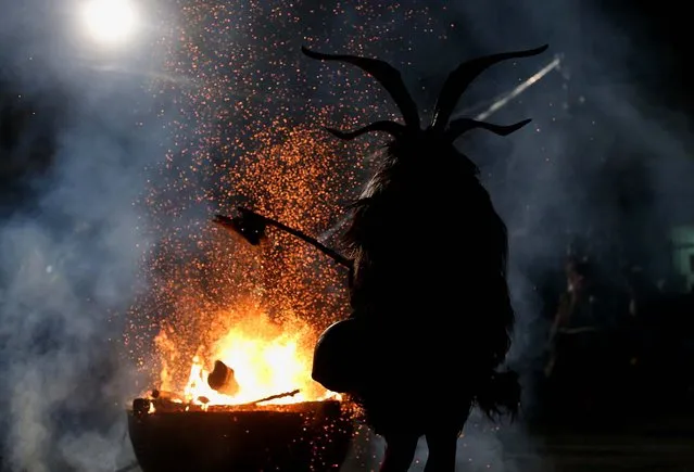 A member of the Haiminger Krampusgruppe dressed as the Krampus creature hits a fire to release sparks on the town square during their annual Krampus night in Haiming. (Photo by Sean Gallup)
