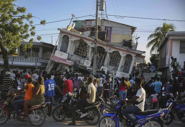 People gather outside the Petit Pas Hotel, destroyed by the earthquake in Les Cayes, Haiti, Saturday, August 14, 2021. A 7.2 magnitude earthquake struck Haiti on Saturday, with the epicenter about 125 kilometers (78 miles) west of the capital of Port-au-Prince, the US Geological Survey said. (Photo by Joseph Odelyn/AP Photo)