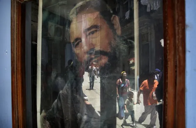 In this May 15, 2015 file photo, pedestrians are reflected in a post office window where a poster of Fidel Castro hangs in Havana, Cuba. (Photo by Desmond Boylan/AP Photo)