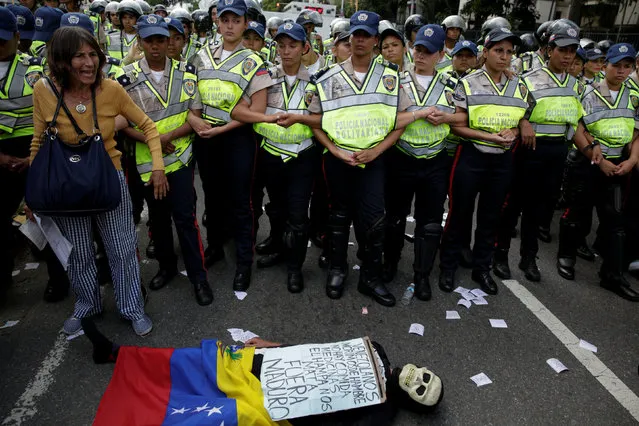 An opposition supporter wearing a costume lies on the ground in front of riot police during a rally against Venezuelan President Nicolas Maduro's government and to commemorate the 59th anniversary of the end of the dictatorship of Marcos Perez Jimenez in Caracas, Venezuela January 23, 2017. The sign reads “Venezuelans starve. There is no food or medicine. The underworld kills us. Get out Maduro”. (Photo by Marco Bello/Reuters)