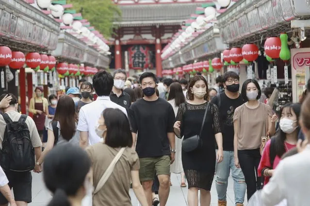People wearing face masks to protect against the spread of the coronavirus walk through the Nakamise main path to the Sensoji temple, lined with shops in the Asakusa neighborhood of Tokyo, Friday, August 13, 2021. (Photo by Koji Sasahara/AP Photo)