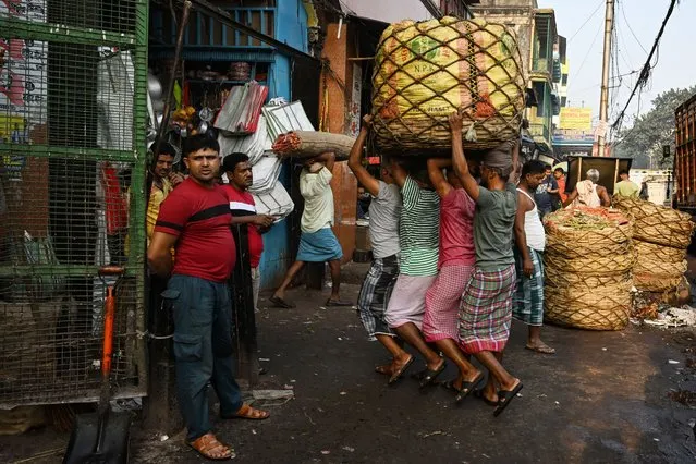 Labourers carry a sack of vegetables at a wholesale market of agricultural products in Kolkata on February 22, 2024. (Photo by Dibyangshu Sarkar/AFP Photo)
