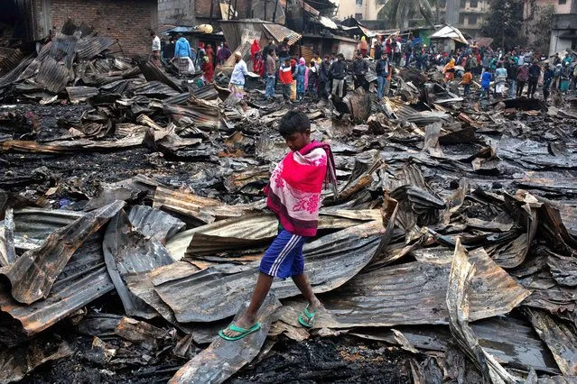 A boy is walking through the debris at Kawranbazar area in Dhaka, Bangladesh on Saturday, January 13, 2024. A woman and a child were killed and four others were injured in a fire at slum. At least 300 shanties were burnt in the fire. (Photo by Md Rakibul Hasan/ZUMA Press Wire/Rex Features/Shutterstock)