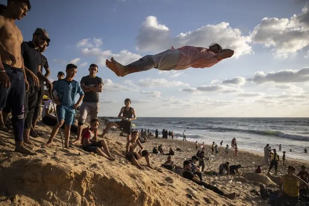 Palestinians watch a man performs acrobatics on the beach of Gaza City, Friday, June 4, 2021. (Photo by Khalil Hamra/AP Photo)