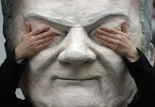 A protester poses with a mask of Olaf Scholz of the German Social Democratic Party (SPD) prior to coalition negotiations of representatives of the German Liberals (FDP), the German Social Democratic Party (SPD) and the German Green Party (Die Gruenen) in Berlin, Germany, Monday, November 15, 2021. (Photo by Michael Sohn/AP Photo)