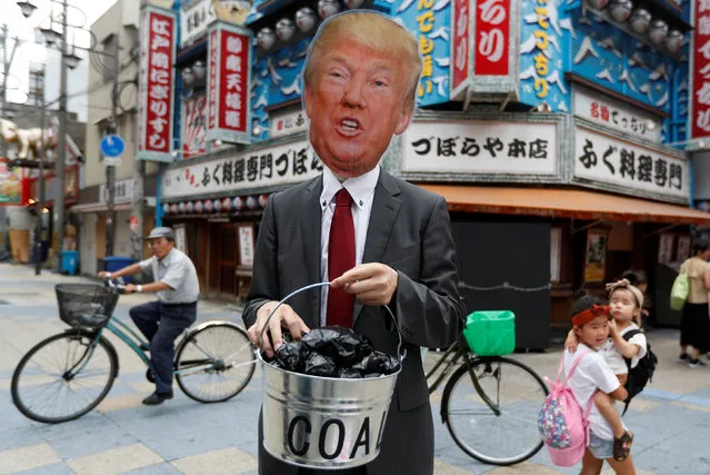 A protester wearing the mask of U.S. President Donald Trump carries a bucket of coal during a demonstration demanding Japan to stop supporting coal at home and overseas, at the G20 Summit in Osaka, Japan, June 28, 2019. (Photo by Jorge Silva/Reuters)
