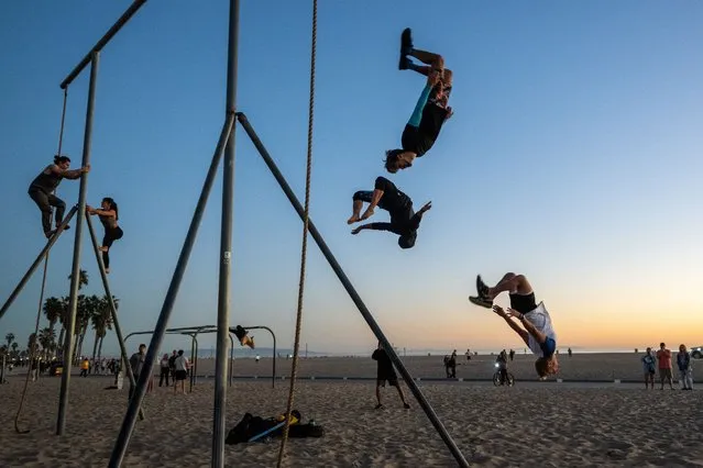 Kyle Soderman, Christian Winchell, and Travis Brewer jump off a pole for a social media video at the Original Muscle Beach in Santa Monica on February 06, 2022 in Los Angeles, California. Large crowds of people flooded to the beach and other outdoor spaces as temperatures reached close to 80 degrees. According to their website, Muscle Beach began in the 1930’s as part of the Works Progress Administration which installed exercise equipment and provided a spot for local body builders and gymnasts to work out. In 1989 the city of Santa Monica renamed it the Original Muscle Beach, so as not to be confused with the one in Venice Beach, and continues to be a workout and gathering spot for gymnasts, acrobats, aerialists, yogis and other like minded individuals. (Photo by Alexi Rosenfeld/Getty Images)