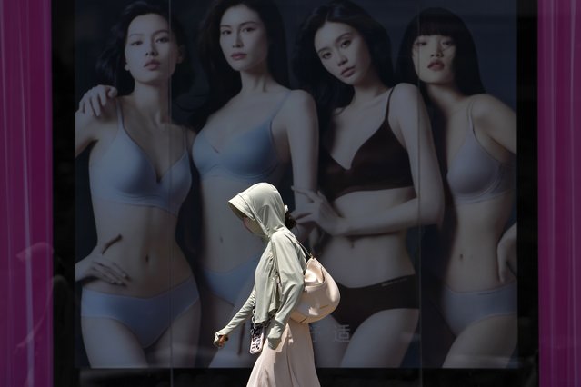 A woman wearing sun protective clothing walks by a lingerie advertisement poster outside a shopping mall on a hot and sunny day in Beijing, Monday, June 17, 2024. (Photo by Andy Wong/AP Photo)