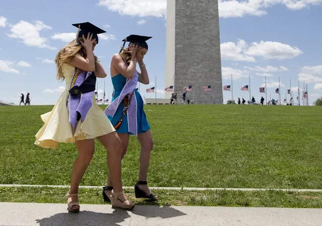 George Washington University graduates Serena Williams, left, and Hannah Raymond, right, struggle against a strong wind as they pose for graduations pictures near the Washington Monument, Sunday, May 15, 2016, in Washington, after their commencement ceremony on the National Mall. (Photo by Carolyn Kaster/AP Photo)