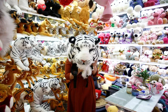 A staff member holds up a toy tiger head as she poses for a picture in a stall at the Yiwu Wholesale Market in Yiwu, Zhejiang province, China, April 28, 2017. (Photo by Thomas Peter/Reuters)