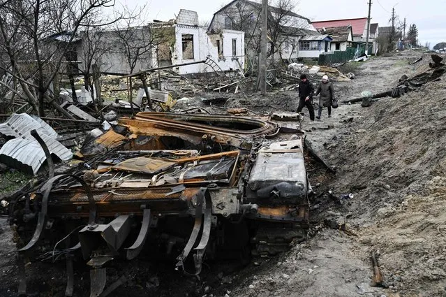 Local residents walk amid debris of a charred Russian tank next to destroyed houses in the village of Zalissya, northeast of Kyiv, on April 19, 2022, during the Russian invasion of Ukraine. (Photo by Genya Savilov/AFP Photo)