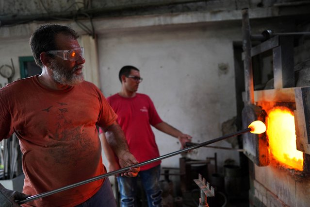 Glassmaker Eduardo Viciana takes a glass out of a furnace in his atelier in Havana, Cuba, on June 21, 2024. (Photo by Alexandre Meneghini/Reuters)