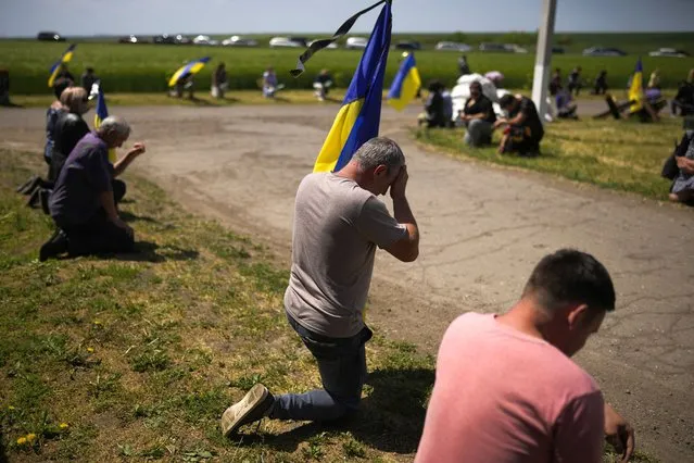 Mourners kneel as they await the coffin of Volodymyr Losev, 38, to pass by during his funeral in Zorya Truda, Odesa region, Ukraine, Monday, May 16, 2022. Volodymyr Losev, a Ukrainian volunteer soldier, was killed May 7 when the military vehicle he was driving ran over a mine in eastern Ukraine. (Photo by Francisco Seco/AP Photo)