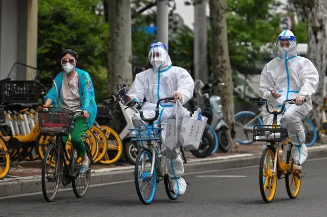 Workers wearing personal protective equipment (PPE) cycle on a street during a Covid-19 coronavirus lockdown in the Jing'an district of Shanghai on May 29, 2022. (Photo by Hector Retamal/AFP Photo)