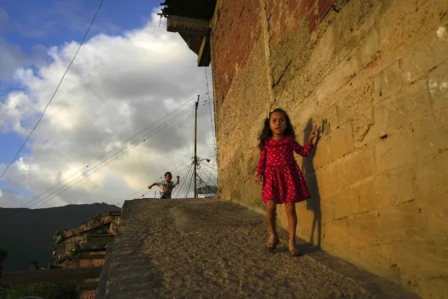 A girl walks down a hill as a boy runs behind during sunset in the Catia neighborhood of Caracas, Venezuela, Saturday, June 4, 2022. (Photo by Matias Delacroix/AP Photo)