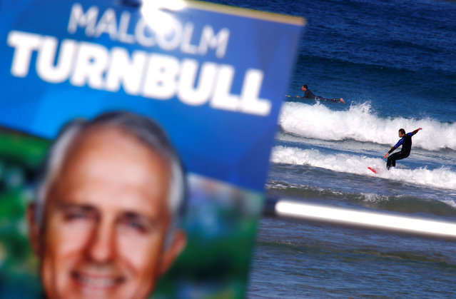 A surfer rides a wave behind a poster promoting the Australian Prime Minister Malcolm Turnbull in front of a voting station, located in the Bondi Surf Lifesaving Club, at Sydney's Bondi Beach, Australia, July 2, 2016. (Photo by David Gray/Reuters)