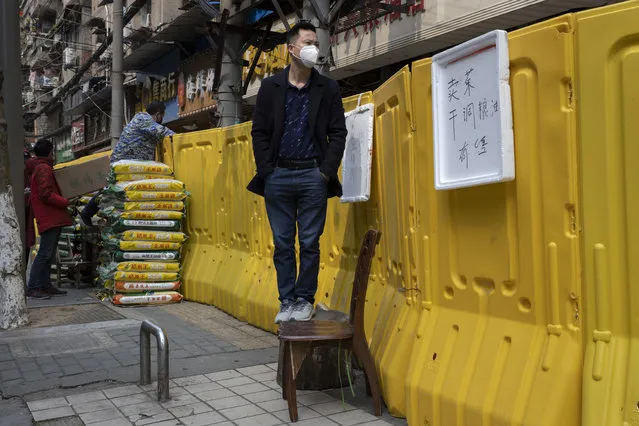 A resident wearing a mask to protect against the spread of the coronavirus looks over barriers used to seal off a neighborhood in Wuhan in central China's Hubei province on Friday, April 3, 2020. Sidewalk vendors wearing face masks and gloves sold pork, tomatoes, carrots and other vegetables to shoppers Friday in the Chinese city where the coronavirus pandemic began as workers prepared for a national memorial this weekend for health workers and others who died in the outbreak. (Photo by Ng Han Guan/AP Photo)