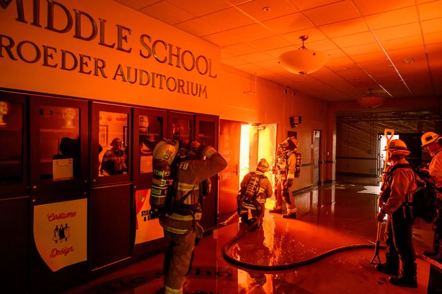 Firefighters prepare to fight flames from inside Eliot Arts Magnet Middle School auditorium as the school burns during the Eaton fire in the Altadena area of Los Angeles county, California on January 8, 2025. At least five people are now known to have died in wildfires raging around Los Angeles, with more deaths feared, law enforcement said January 8, as terrifying blazes leveled whole streets, torching cars and houses in minutes. More than 1,000 buildings have burned in multiple wildfires that have erupted around America's second biggest city, forcing tens of thousands of people from their homes. (Photo by Josh Edelson/AFP Photo)
