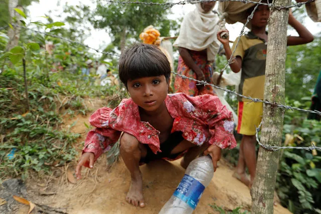 A Rohingya refugee girl who crossed the border from Myanmar two days before, crawls under a barbed wire during her walk to the Kotupalang refugee camp near Cox's Bazar in Bangladesh on October 19, 2017. (Photo by Jorge Silva/Reuters)